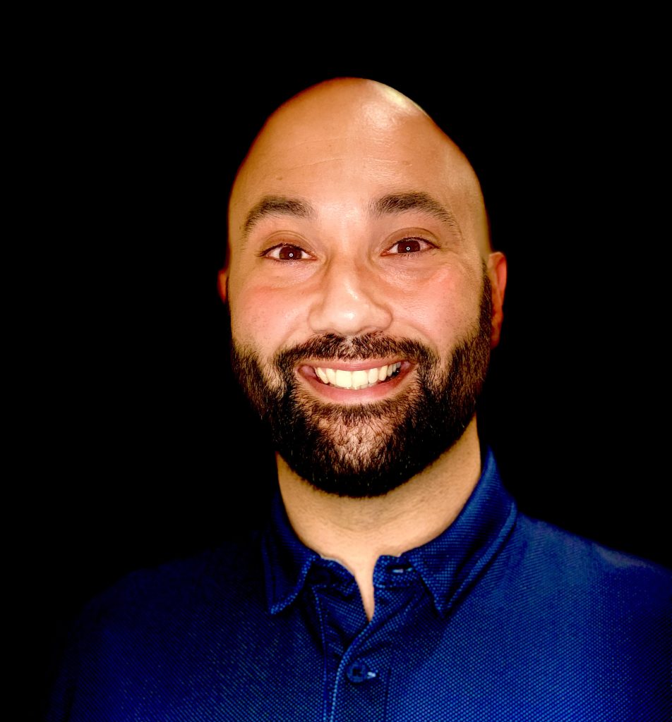 Brett Roer Headshot, smiling with black background.