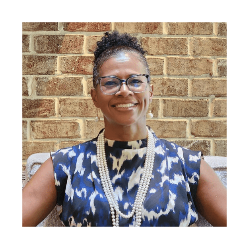 Casidy Sanders smiling and seated on a wicker chair against a brick wall background