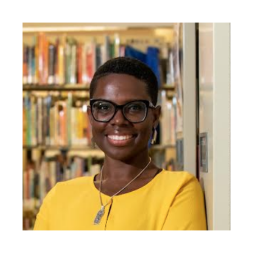 Dr. Vanessa Prosper with short hair wearing glasses and a yellow blouse standing in front of a bookshelf.