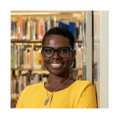 Dr. Vanessa Prosper with short hair wearing glasses and a yellow blouse standing in front of a bookshelf.