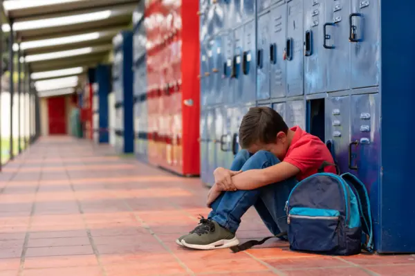 a student in an empty hallway, sitting on the ground with their head looking down to embody crisis management for schools