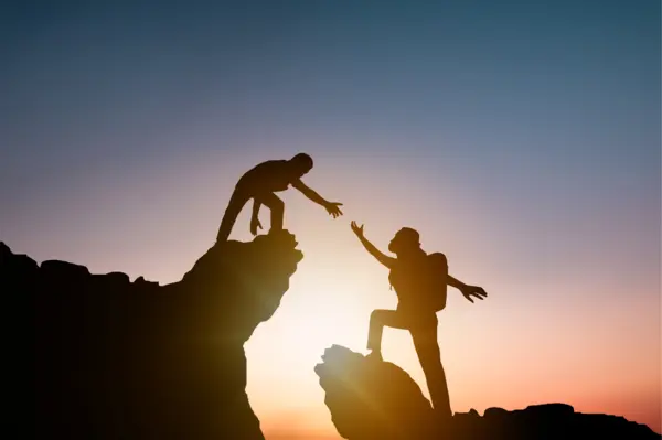 Two people, one heling the other traverse a small crevasse on a mountain embodying the importance of supporting deans in schools